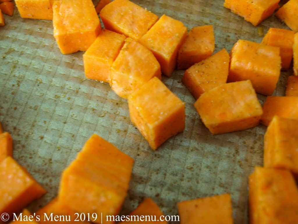 Seasoned cubed sweet potato chunks on an oiled gold baking sheet.