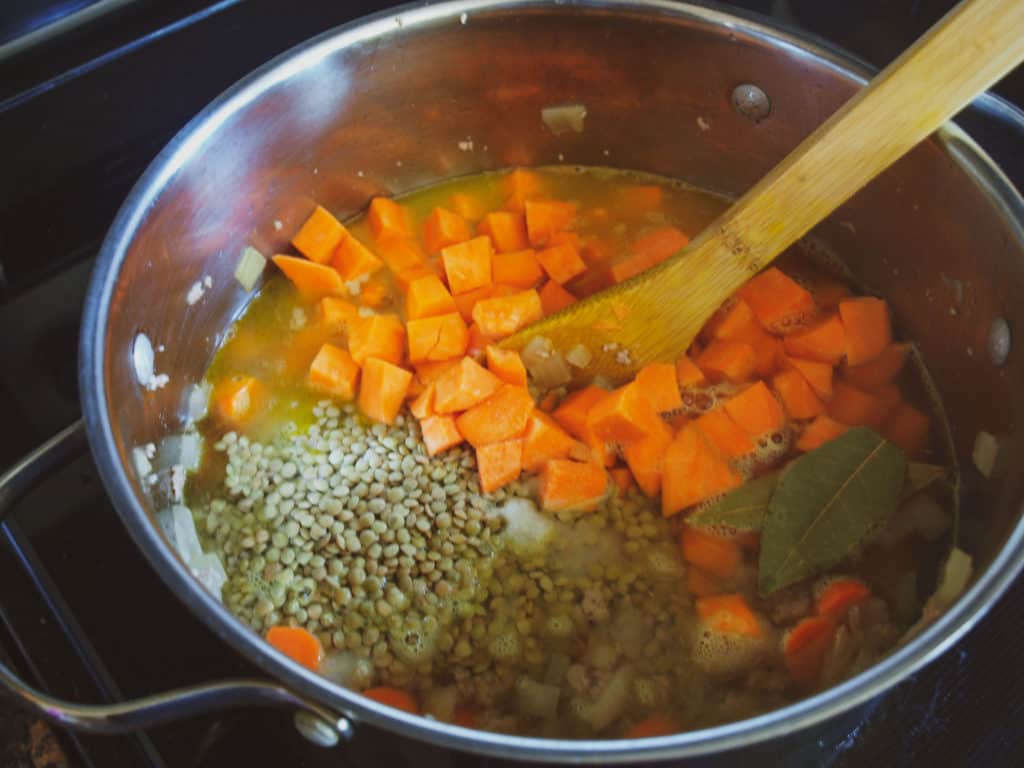 Stock pot with sweet potatoes, lentils, bay leaves, and veggies cooking to make Moroccan Turkey Lentil Soup