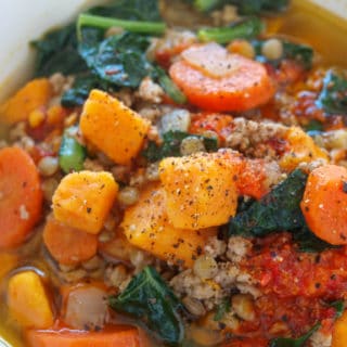 Moroccan sweet potato and lentil soup with kale and carrots in a large white soup bowl.