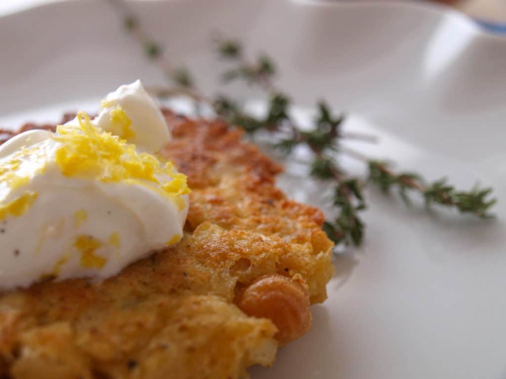An Easter dinner side Garbanzo Bean Fritter with sour cream and lemon zest sitting on a white plate with thyme.