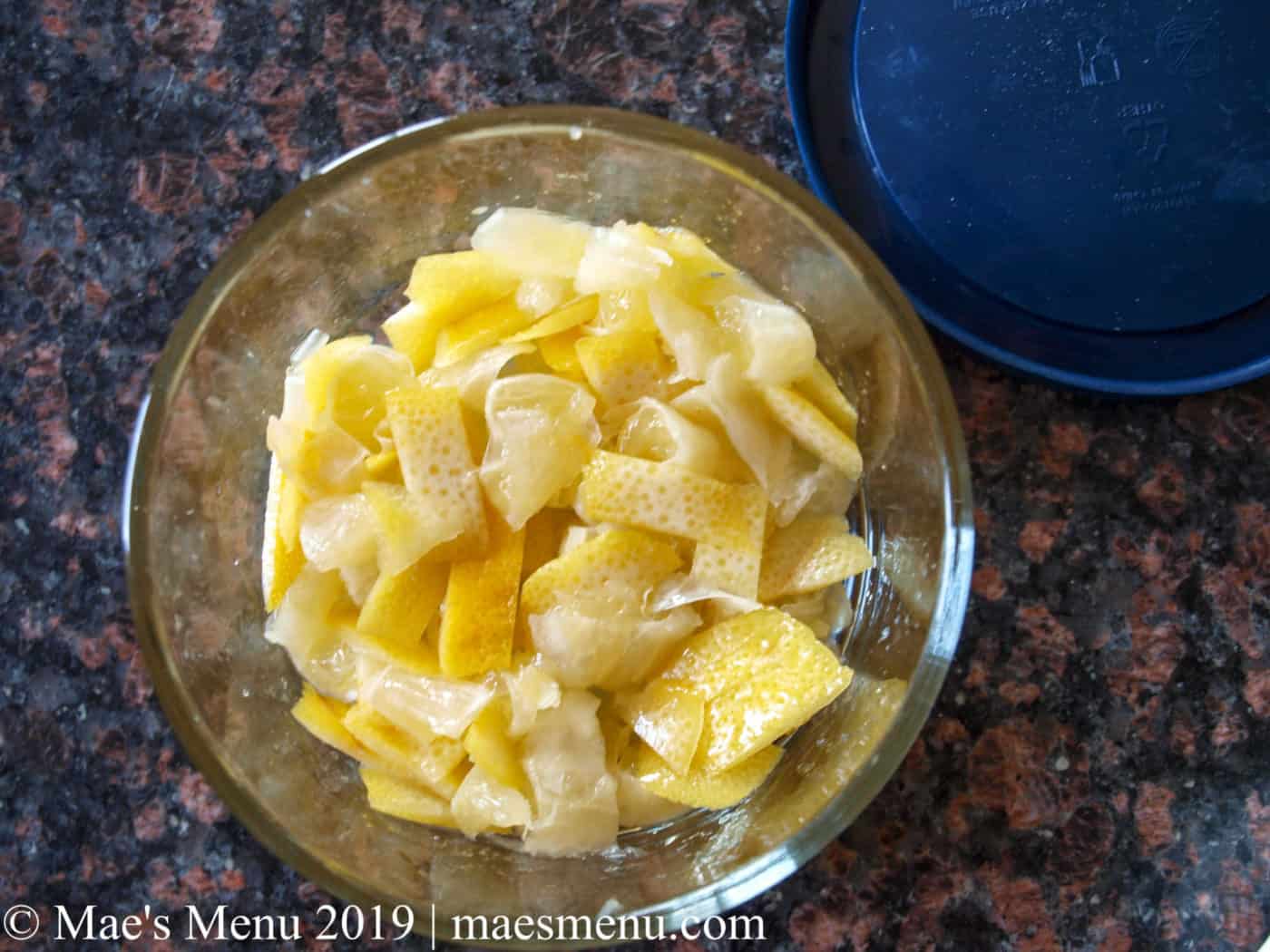 Quick Preserved Lemons in a glass bowl on a black granite counter. Blue lid to the bowl on the counter next to the bowl.