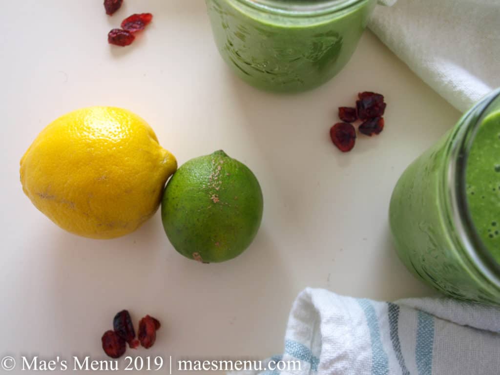 Two glasses of Pineapple Green Smoothie, some citrus, and dried cranberries.