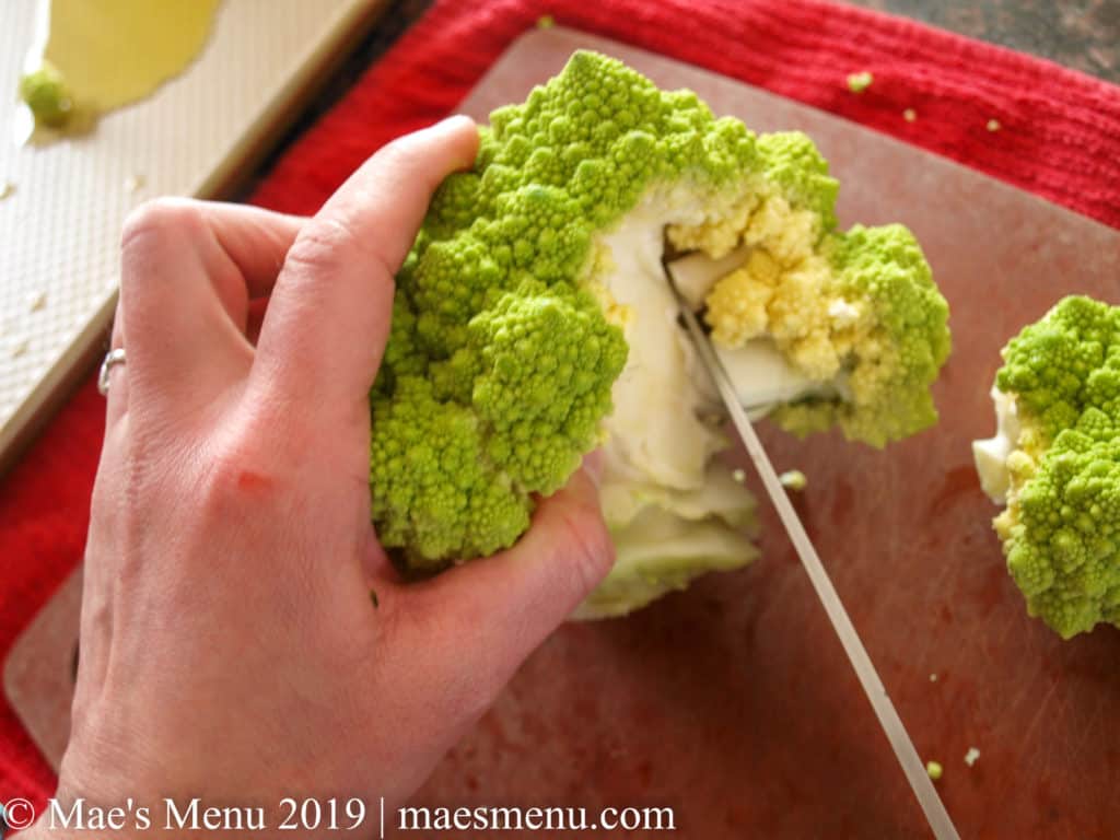 Cutting up a romanesco cauliflower on a brown cutting board and red back ground.