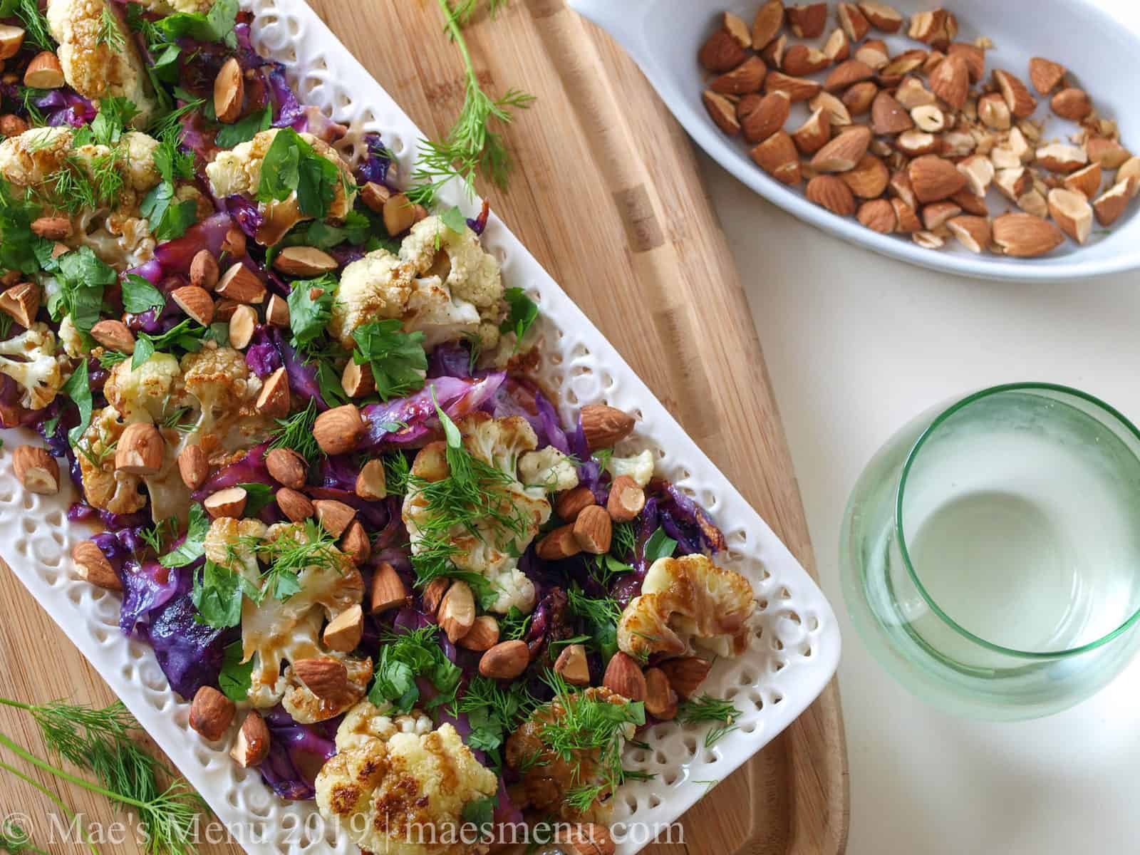 Platter of Roasted Cauliflower & Cabbage Salad Recipe with a glass of sparkling water and dish of roasted nuts.