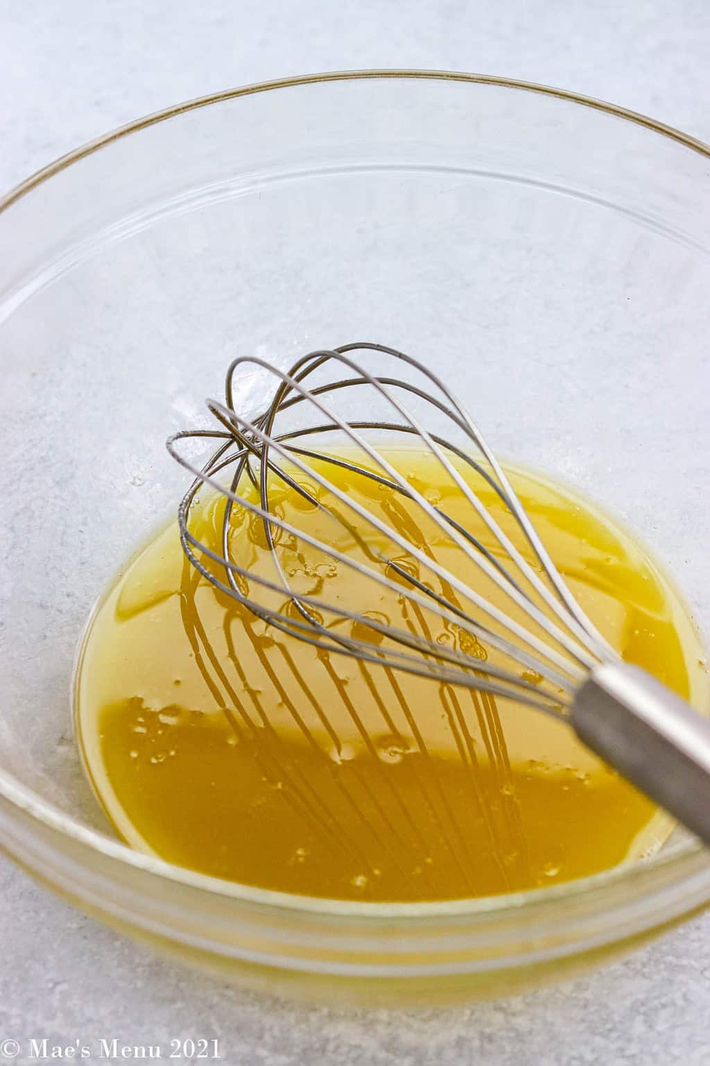 A whisk in a clear bowl with salad dressing