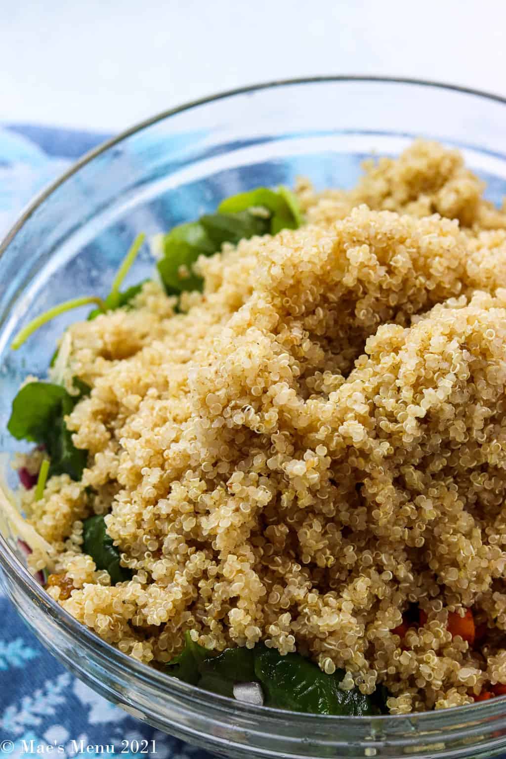A large mixing bowl with quinoa and greens on the bottom