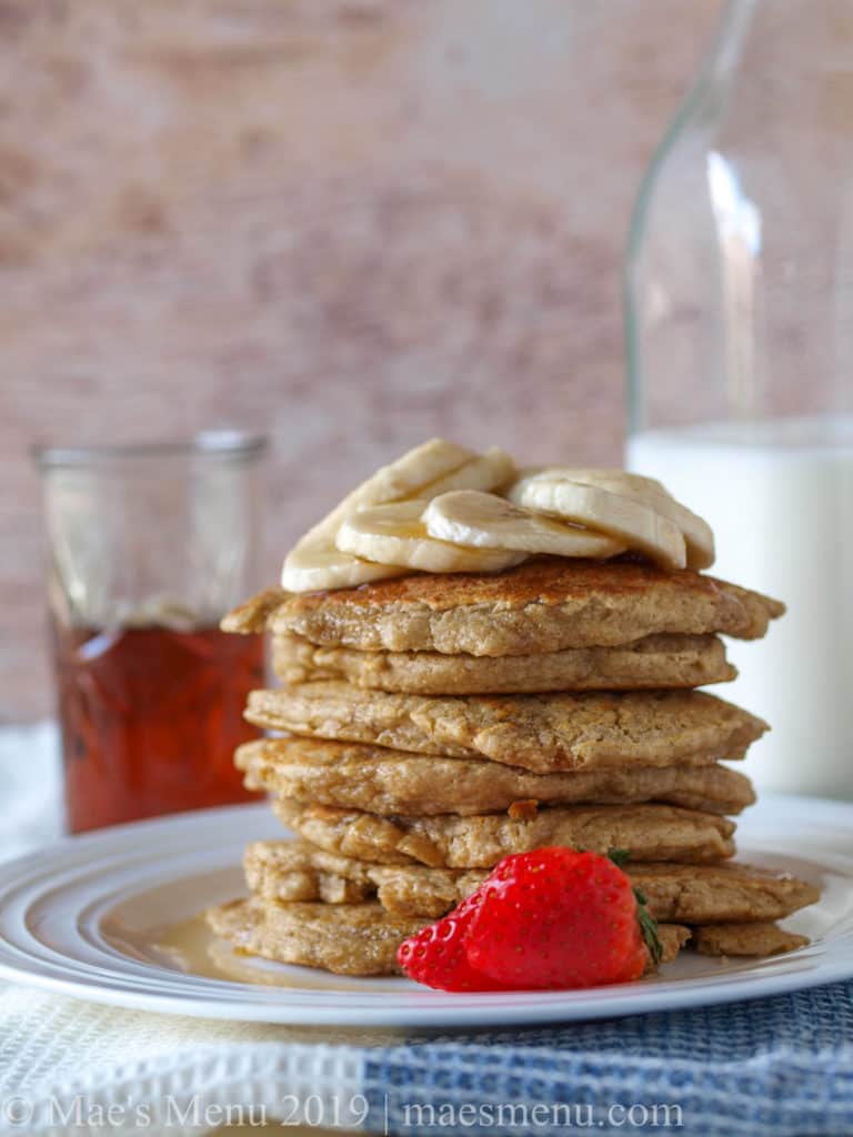 A stack of pancakes in front of a jar of maple syrup and milk