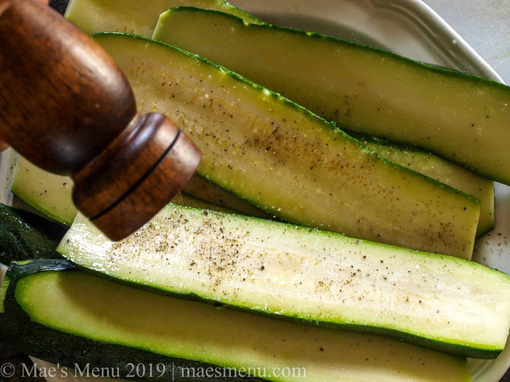 Seasoning the zucchini slices with oil, salt, and pepper.