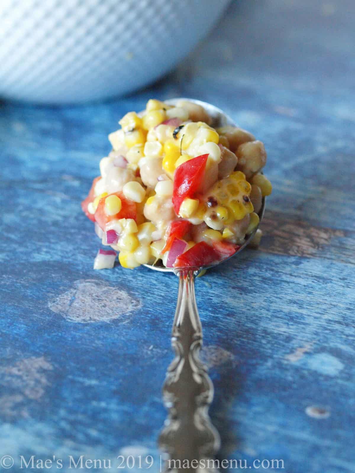 Large spoon full of Chickpea & Grilled Corn Salad with Roasted Garlic Salad Dressing.