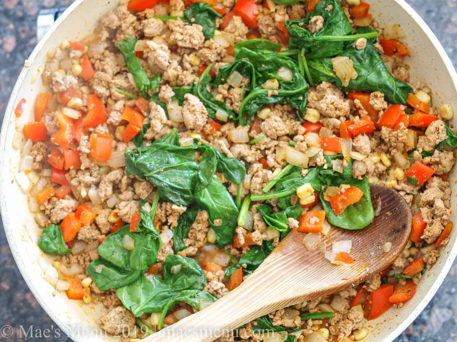 Turkey, sweet peppers, onion, spinach, and corn cooking in a non stick skillet. 
