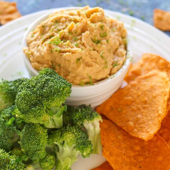 A small crock of curry hummus with sweet potato chips and broccoli.