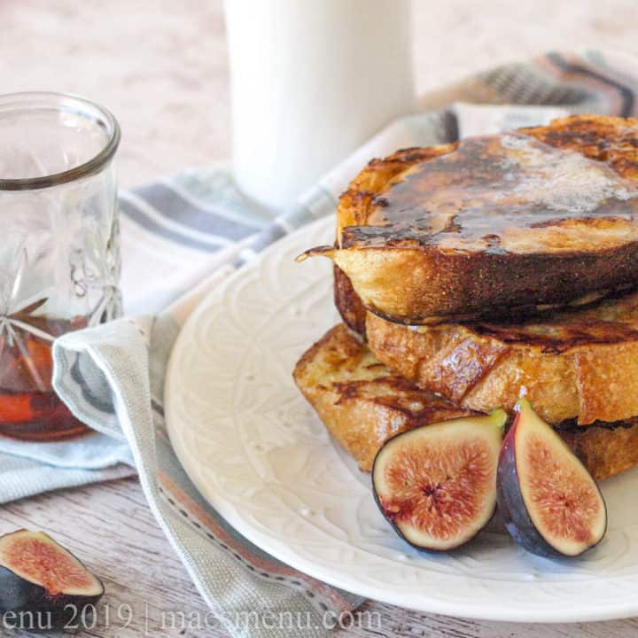 A stack of classic french toast next to figs, maple syrup, and a glass of milk.