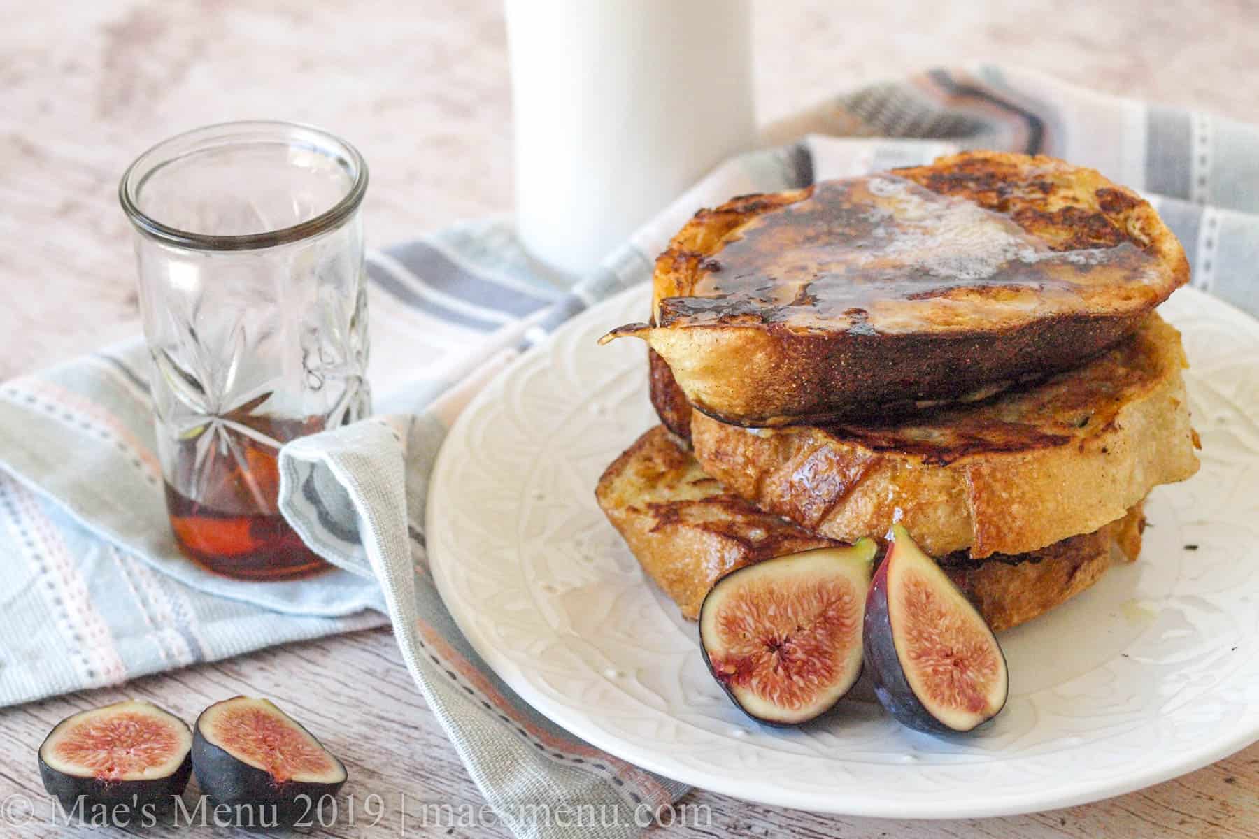 A stack of classic french toast next to figs, maple syrup, and a glass of milk.