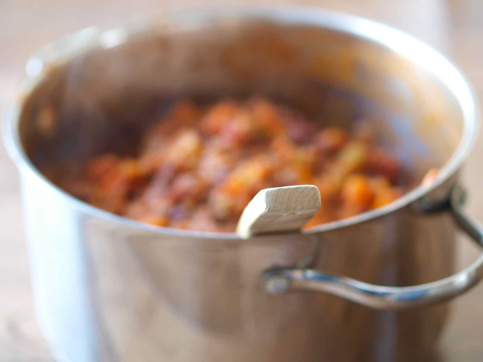 A slightly out of focus large pot of jackfruit chili with a wooden spoon sticking out the side 