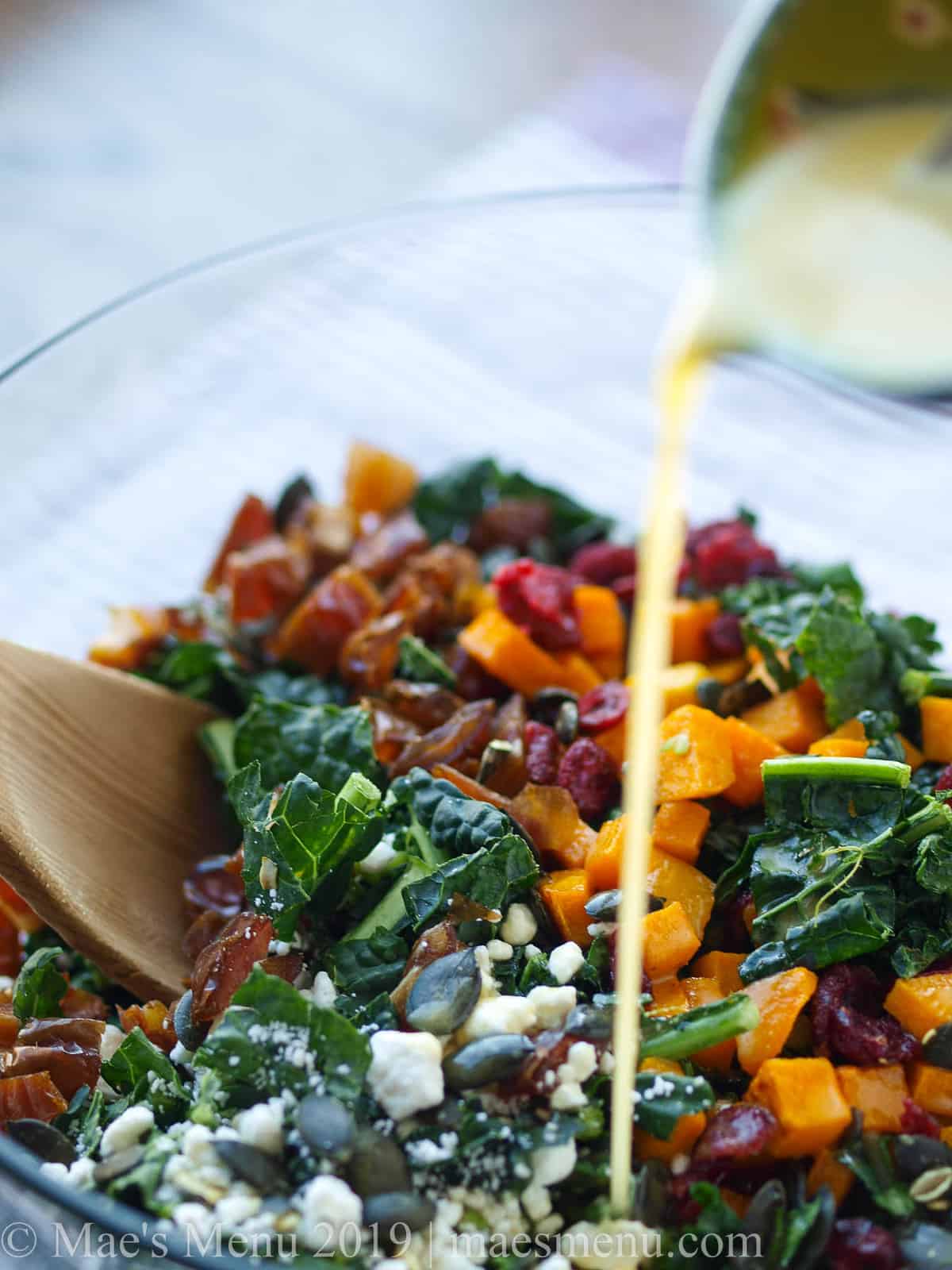 A bowl of Holiday lacinato kale salad with citrus agave dressing drizzling over.