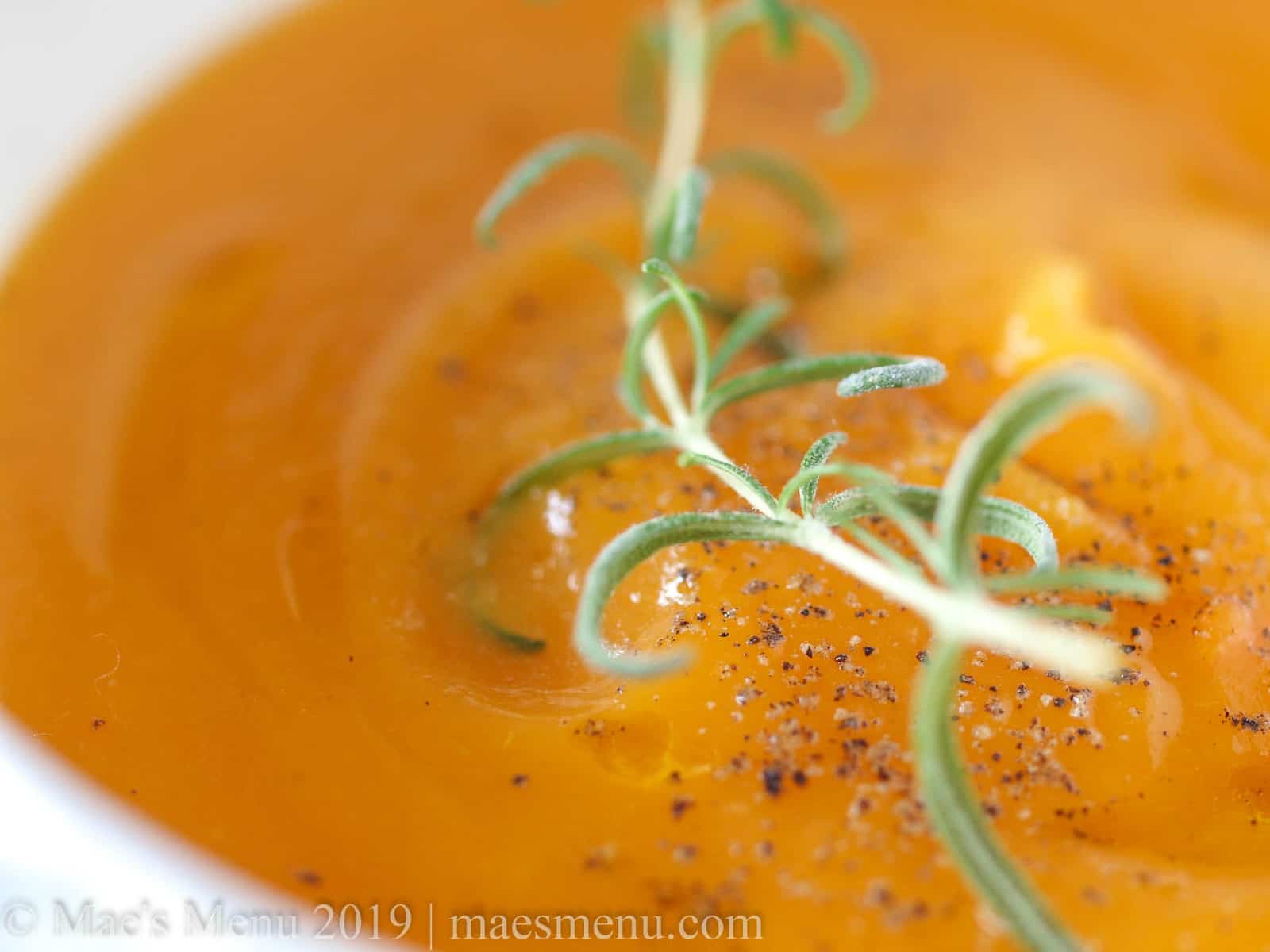 Up-close shot of my vegan butternut squash soup recipe with a sprig of rosemary on top