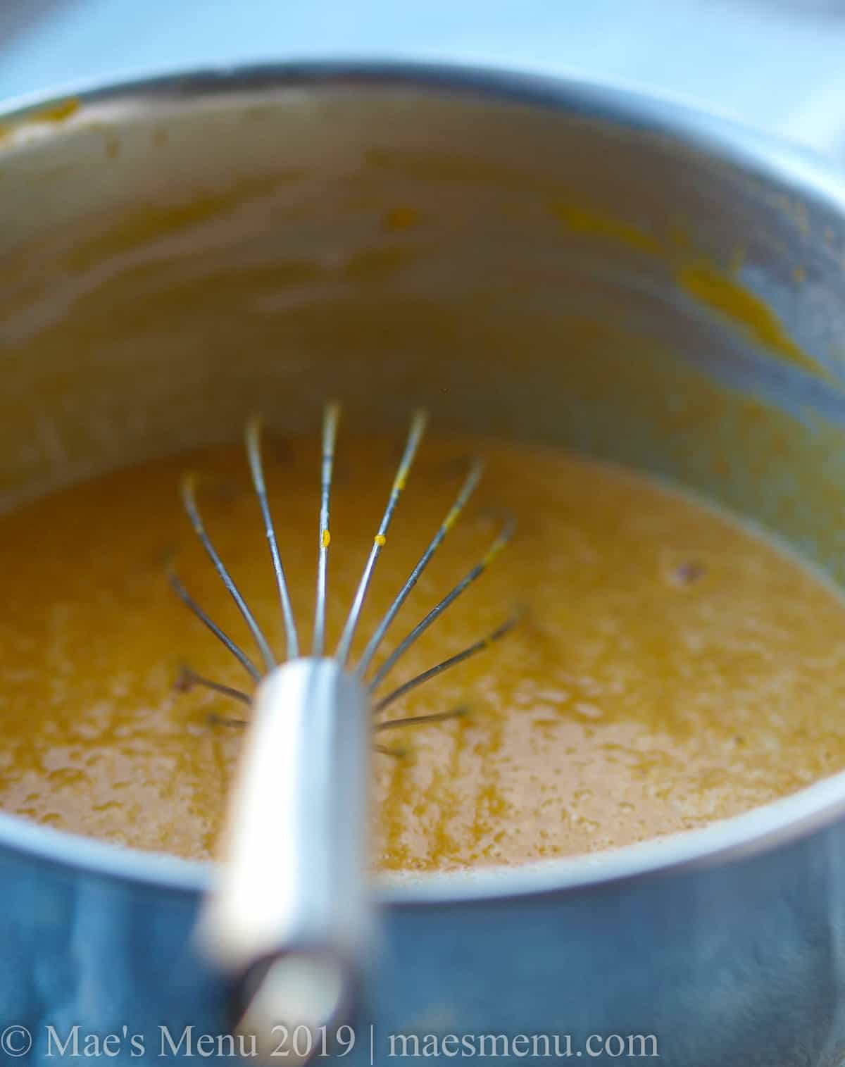 An up-close picture of pumpkin pie filling with a whisk in it.