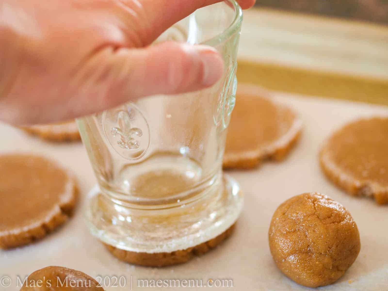 A hand holding a drinking glass and gently pressing down on peanut butter cookies