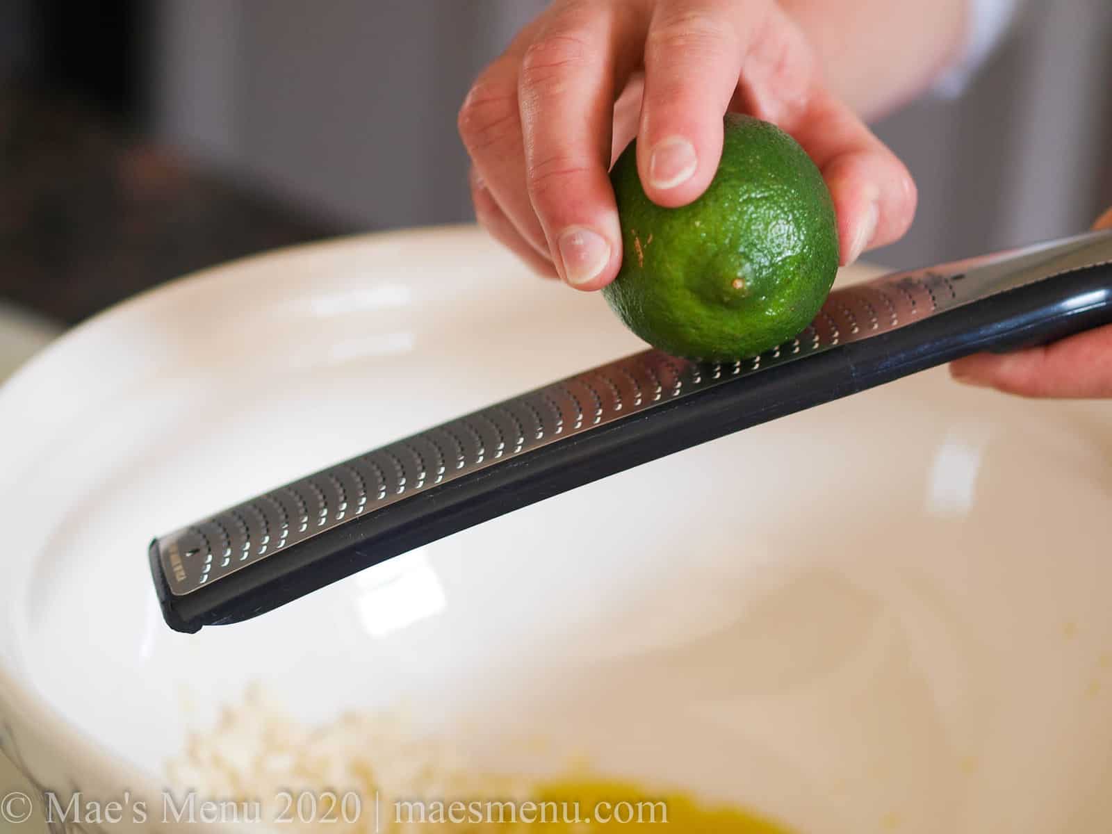 A hand zesting a lime over a large bowl