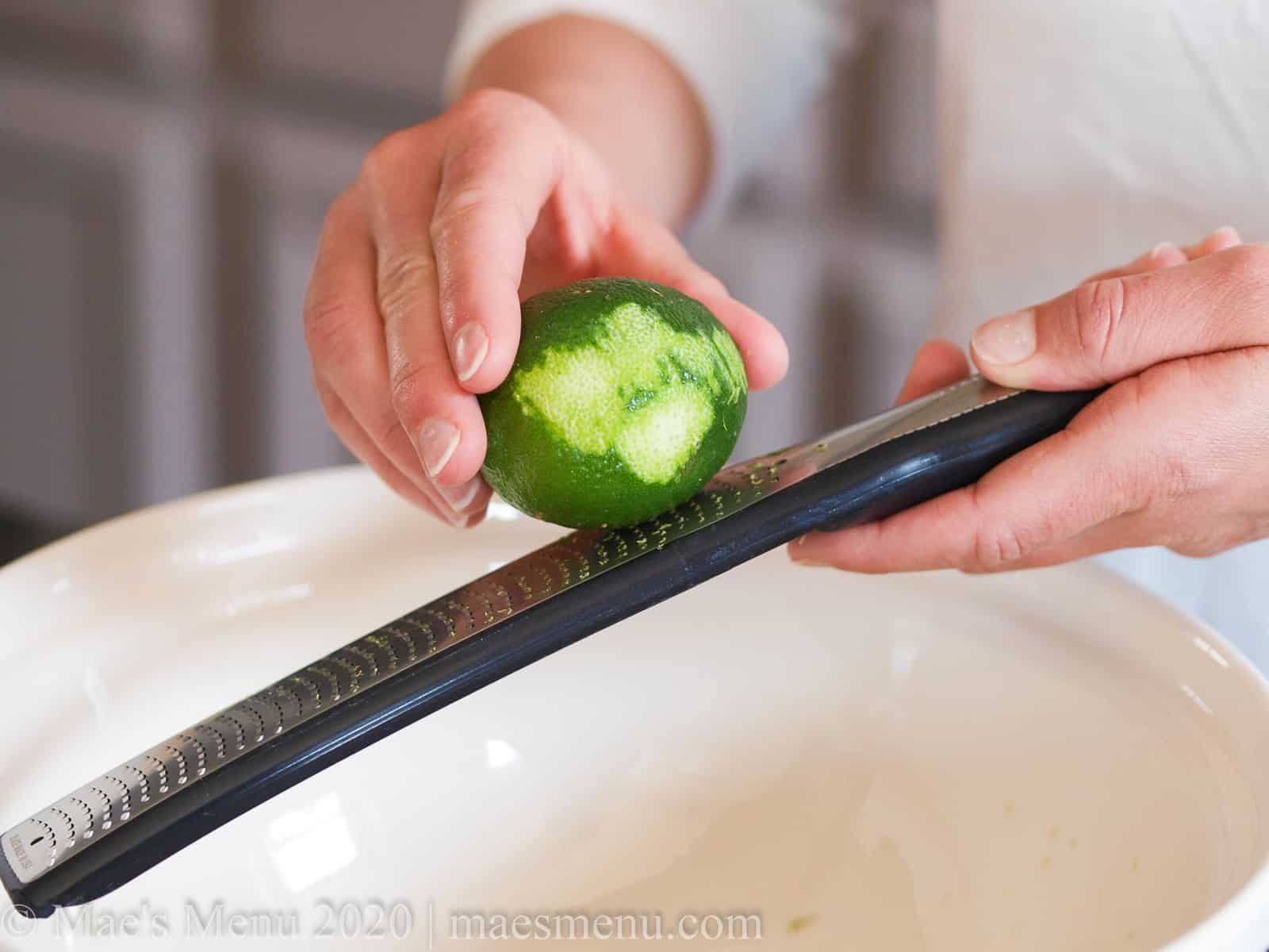 A hand zesting a partial zested lime over a large bowl