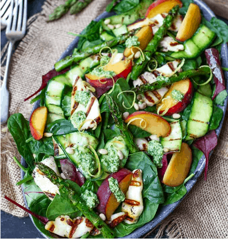 A large blue platter of a salad with peaches, asparagus, and grilled halloumi cheese sitting on top of a brown burlap fabric.