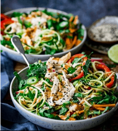 two large bowls of Thai chicken salad on a wooden table with a blue towel next to them.