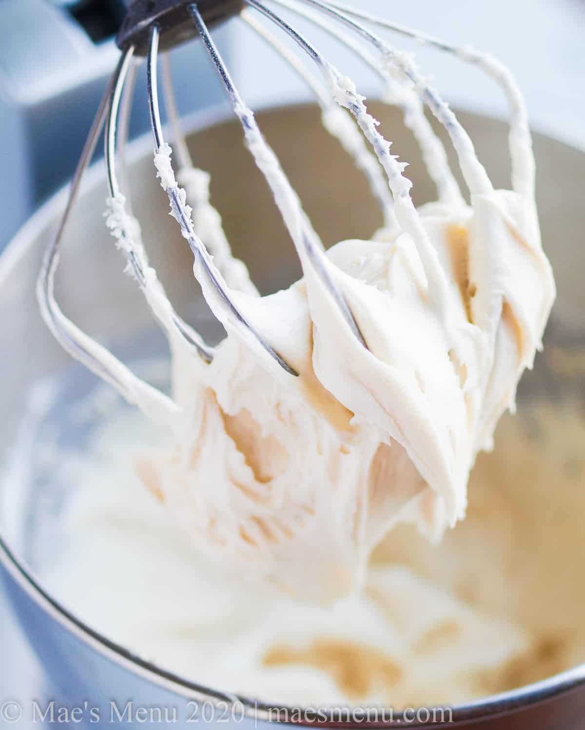 Whisk of a stand mixer covered in cream cheese frosting.