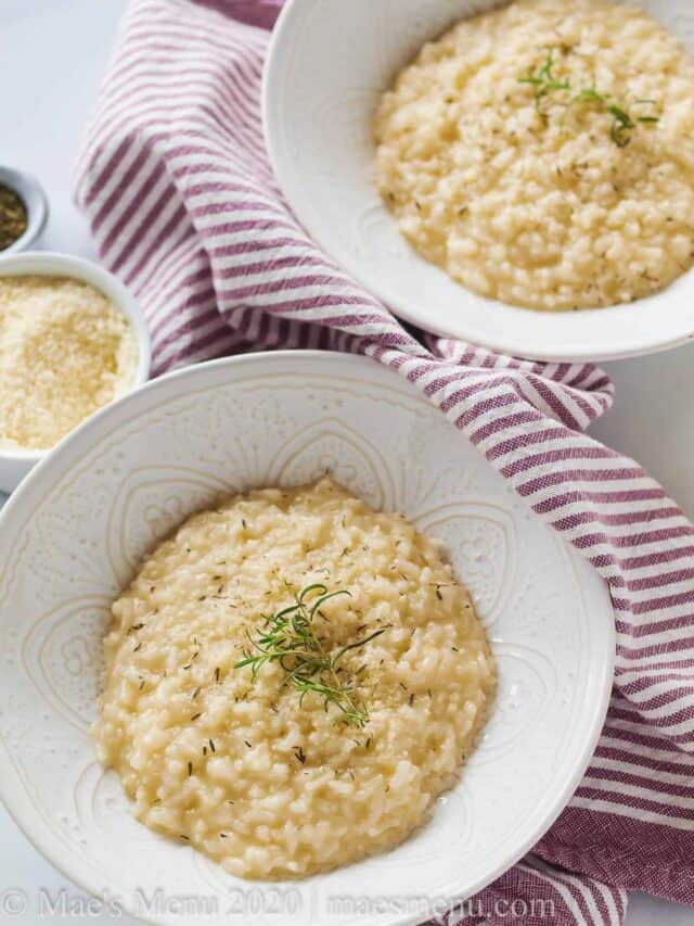 Two bowls of instant pot cheese risotto with herbs on top.