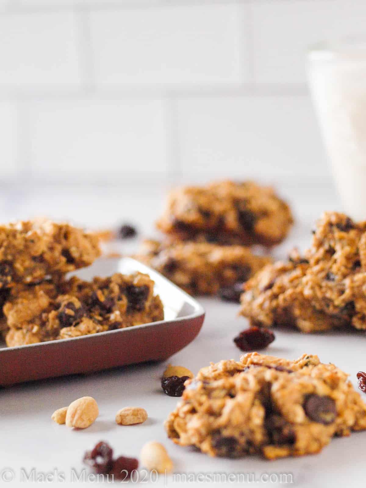 Oatmeal breakfast cookies on a table next to a small plate of cookies, raisins, and peanuts. 