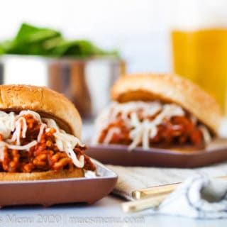 Two turkey sloppy joes on small plates with a glass of beer and a salad behind it.