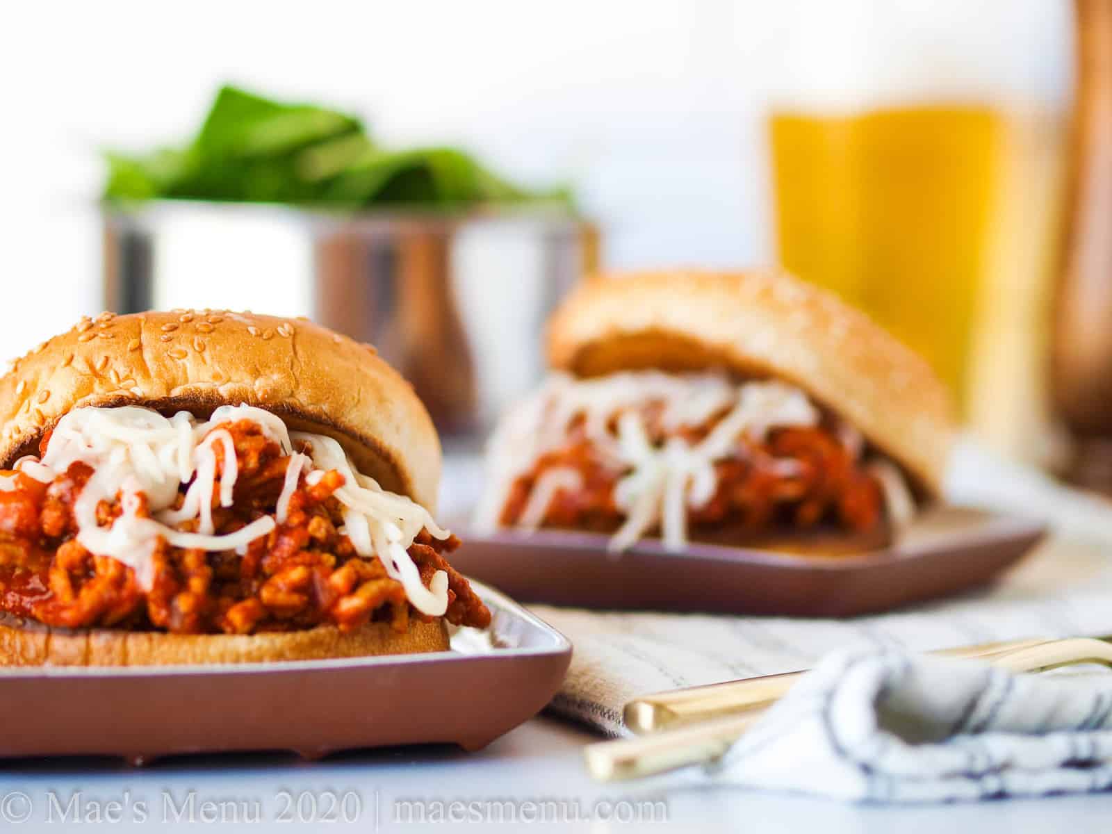 Two turkey sloppy joes on small plates with a glass of beer and a salad behind it.