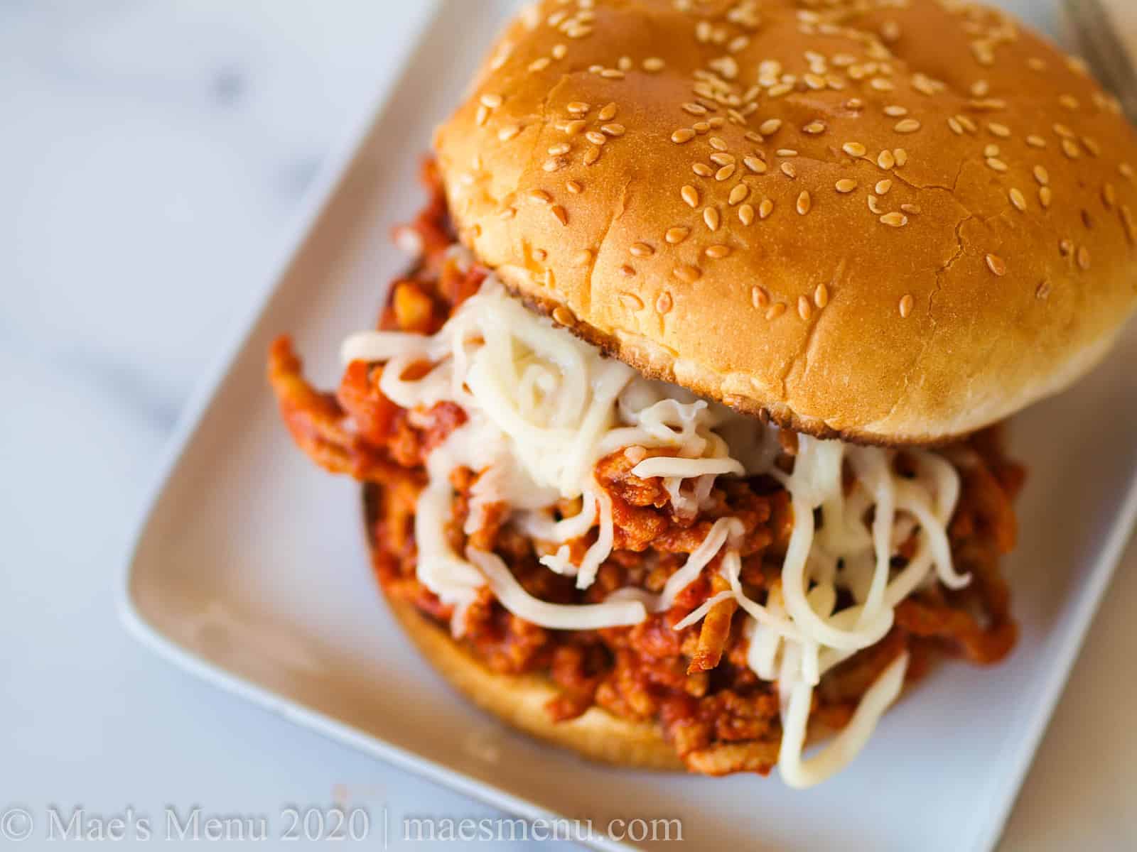 A sloppy joe with shredded cheese on top on a white plate. 