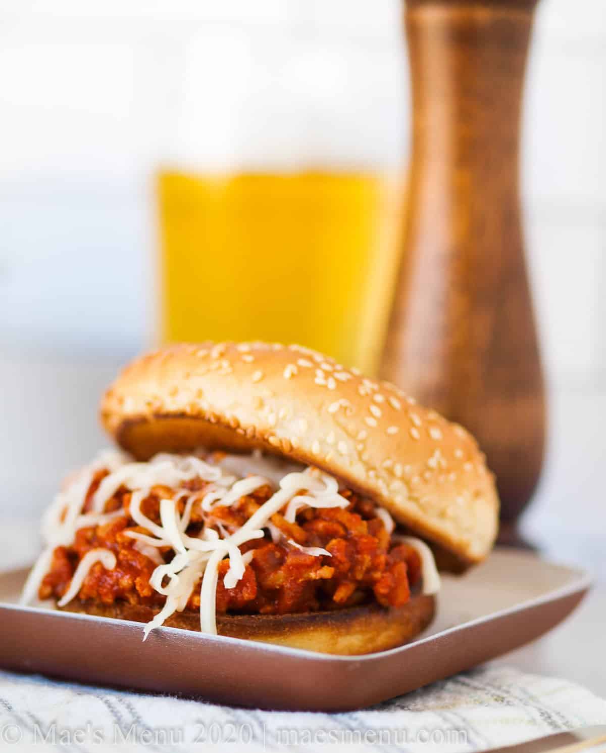 A small dish with a sloppy joe in front of a wooden pepper grinder and a glass of beer