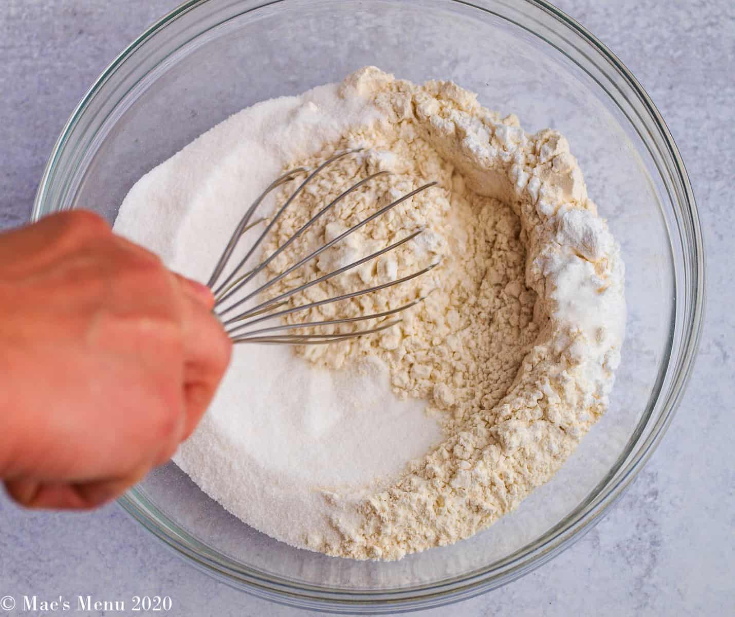 A whisk mixing together flour and sugar in a large bowl