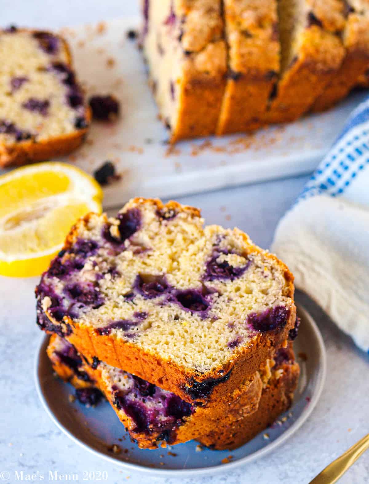 A small dish of lemon blueberry bread with a small cutting board of sliced bread in the back