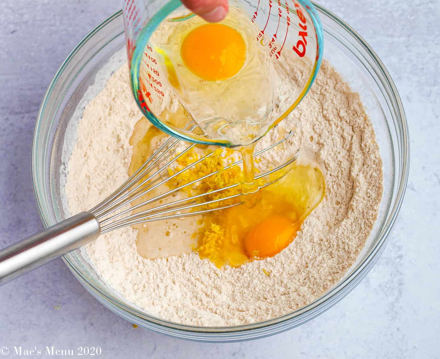 Pouring two eggs into a bowl with flour, sugar, lemon juice, and lemon zest