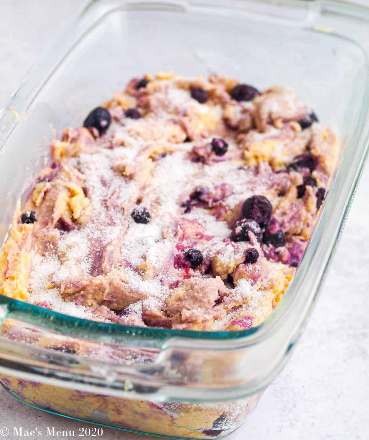 A glass loaf pan filled with blueberry lemon bread batter and sprinkled with sugar