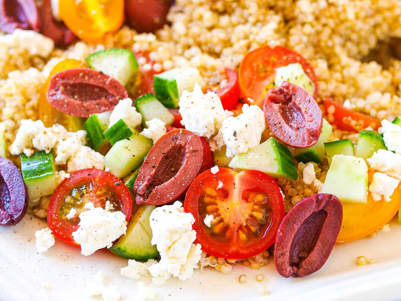 An upclose shot of the olives, tomatoes, cucumbers, sweet peppers, and feta over quinoa