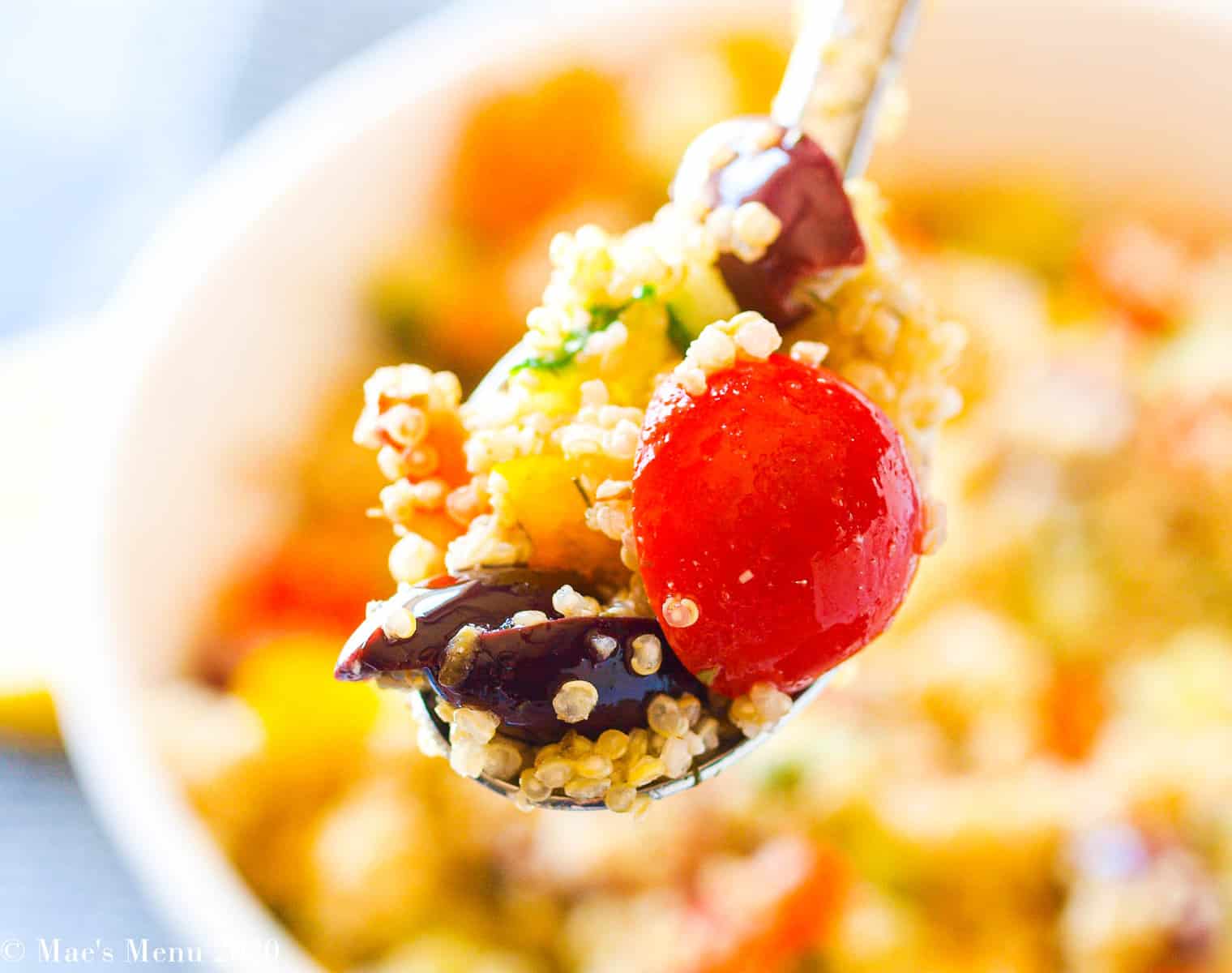 A large spoonful of greek quinoa salad with the rest of the quinoa salad blurred in the background