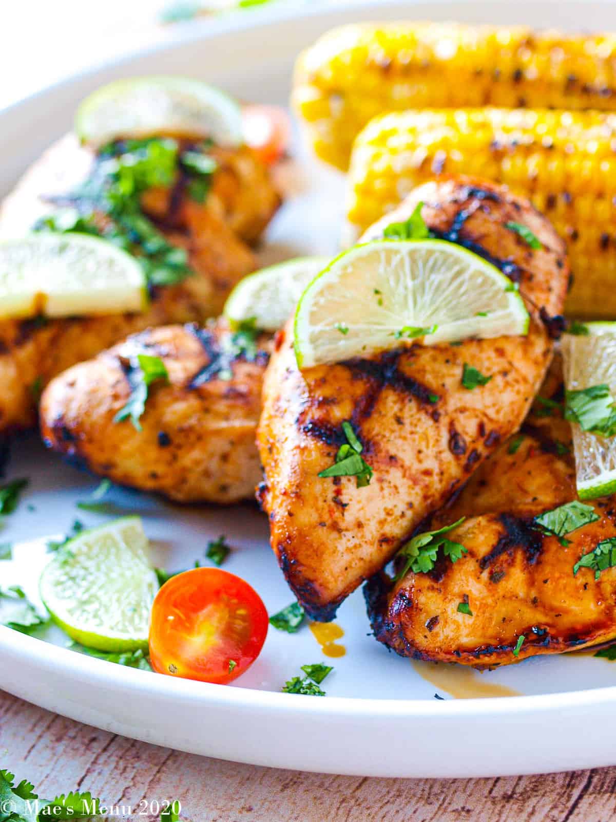 Mexican chicken marinated chicken on a white serving platter with lime wedges, tomatoes, and grilled corn