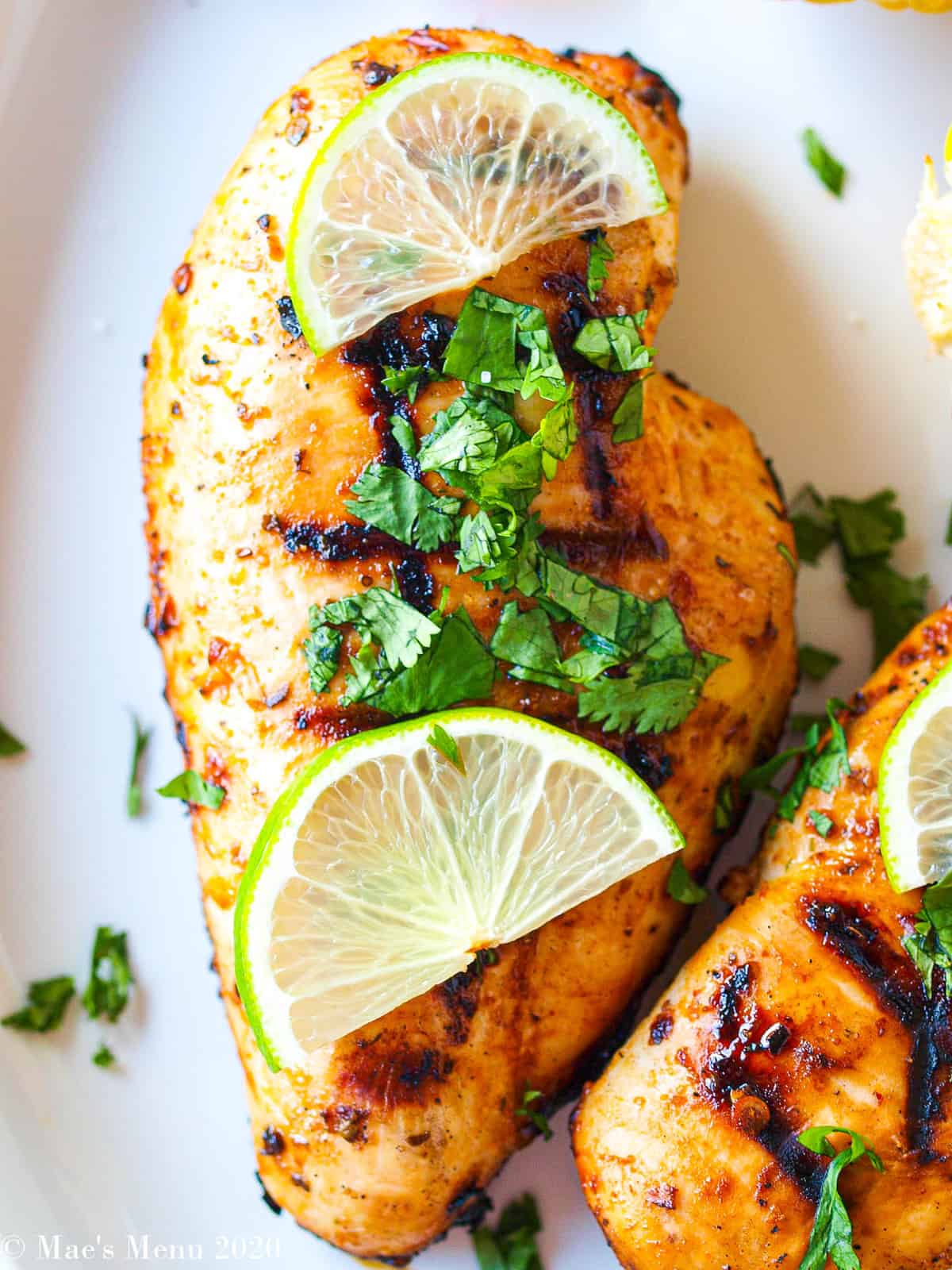 An upclose shot of a grilled chicken breast with chopped cilantro and sliced limes on top. 