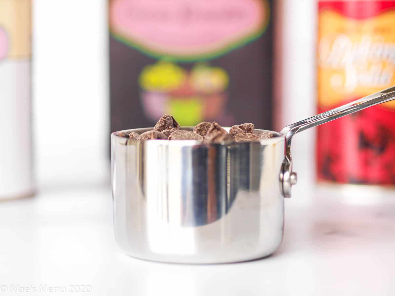 An up-close shot of a measuring cup of chocolate chips with cocoa powder, baking soda, and baking powder in the background.