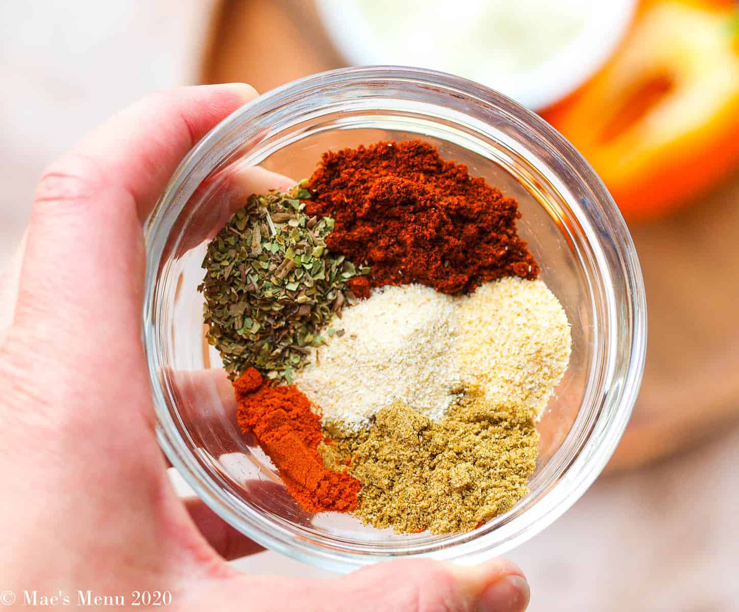 A small clear dish full of taco seasoning spices over a platter of onion and peppers. 