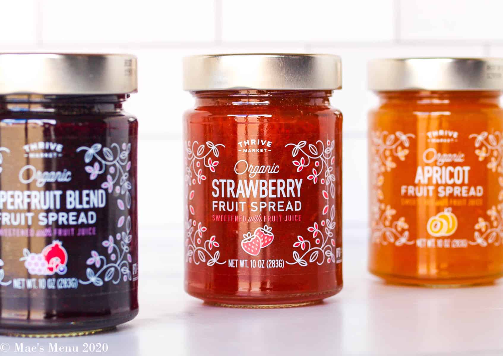 Three jars of thrive market fruit spread lined up on a counter with a white subway tile in the background.