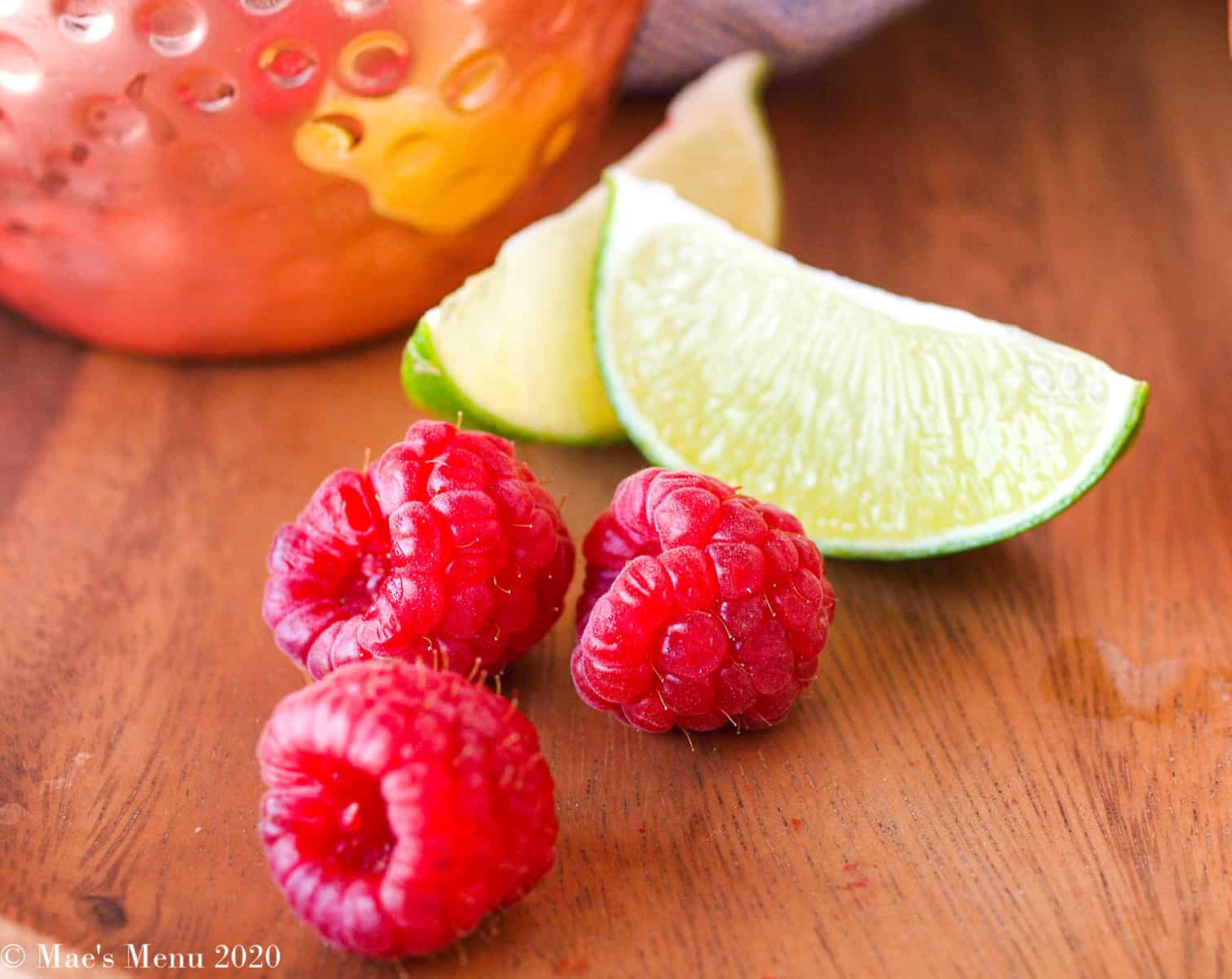 An up-close shot of fresh raspberries and lime slices on a wooden tray