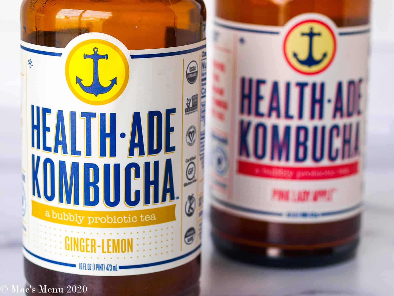 An up-close shot of two bottles of health-ade kombucha: one bottle of ginger lemon an the other of pink lady apple