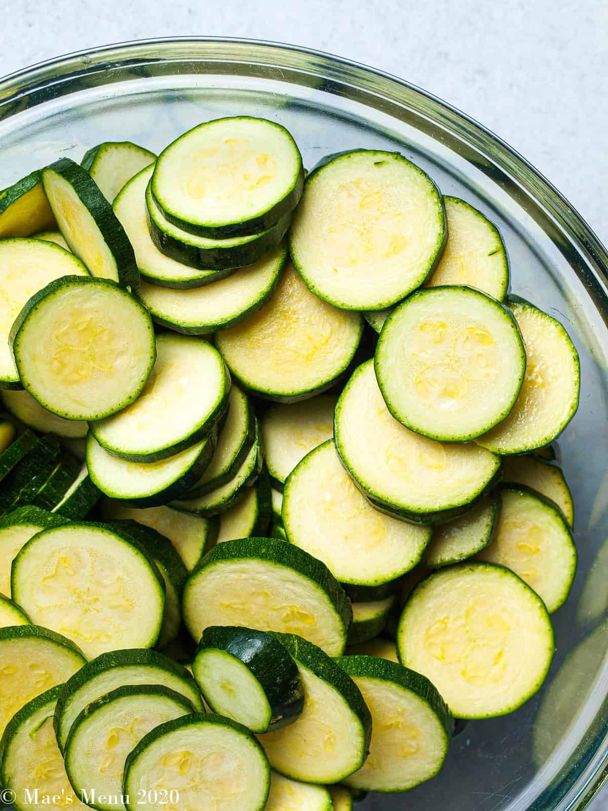 A clear mixing bowl of sliced zucchini coins.