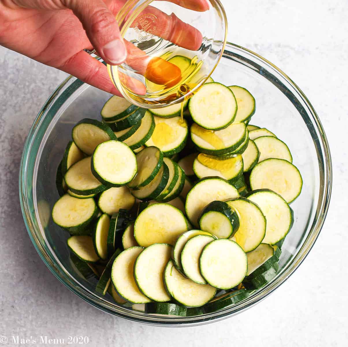 Pouring oil over a glass mixing bowl of zucchini coins