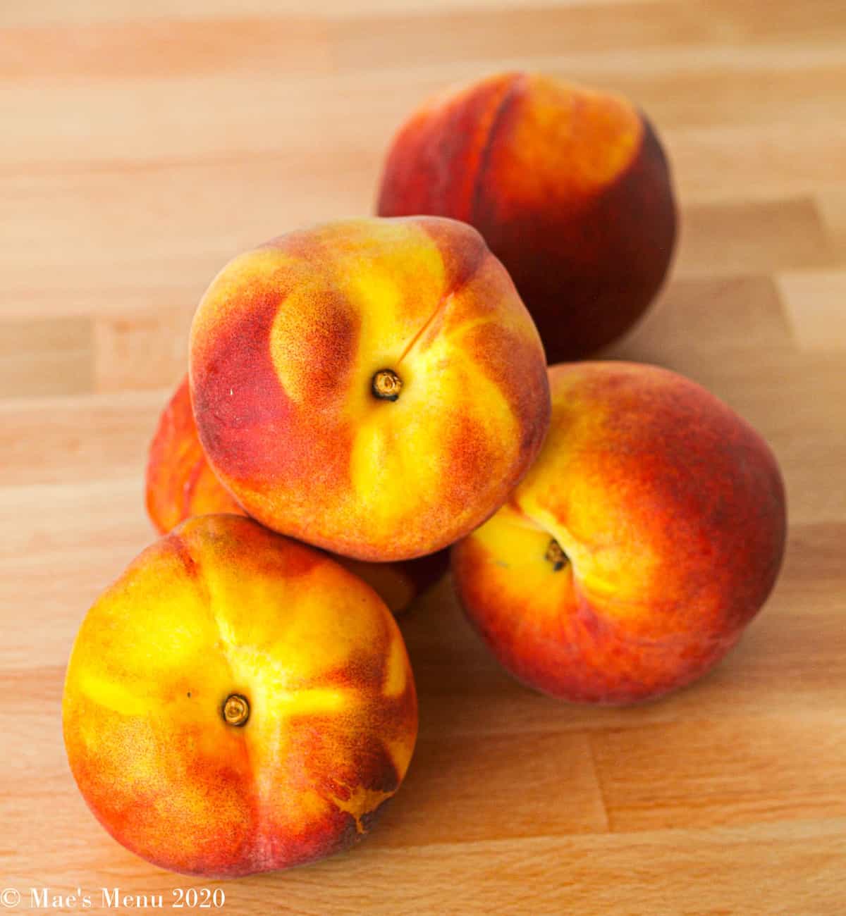 5 peaches sitting on a butcher block counter