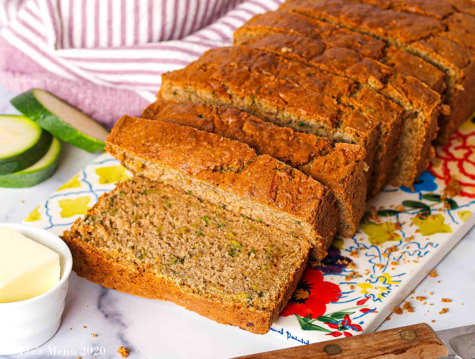 a side shot of a loaf of gluten-free zucchini bread sliced on a flowered platter